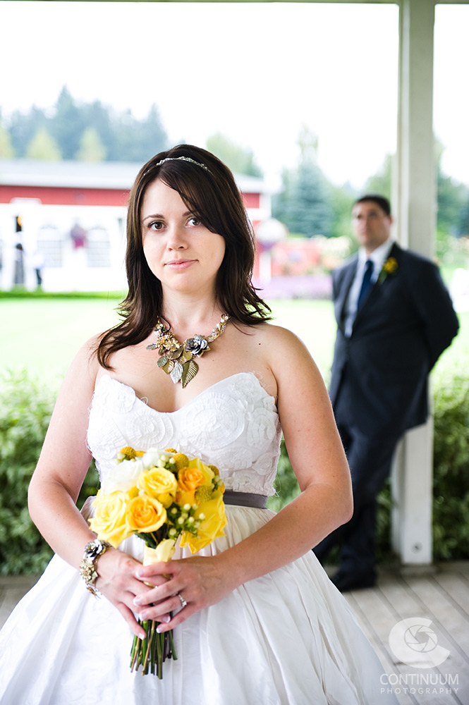 Portrait of bride in handmade gown with vintage jewelry and yellow and white bouquet.