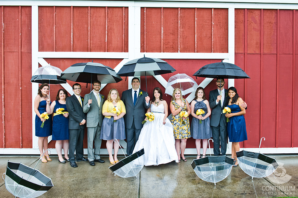 Rainy day bridal party portrait in front of barn with umbrellas.