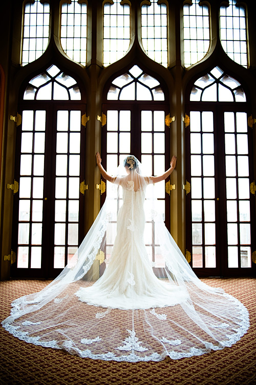 San Diego bride standing in front of ornate windows cathedral length lace veil before her Orange County Wedding.